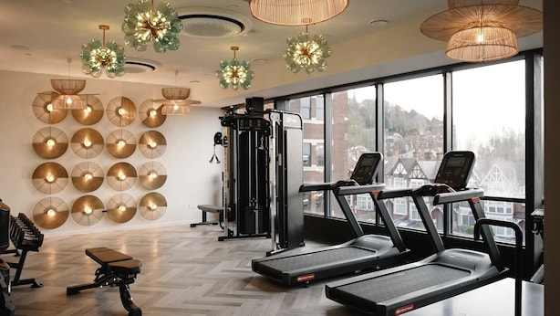 Ein Fitnessstudio mit Laufbändern, Trainingsgeräten und großen Fenstern mit Blick auf die Stadt.