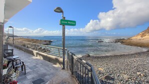 Une vue sur la mer avec une rambarde en métal, un panneau de signalisation et un espace extérieur aménagé avec des chaises et une table.