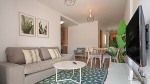 Un salon moderne avec un canapé, une table basse, un téléviseur et des reproductions botaniques encadrées accrochées au mur.