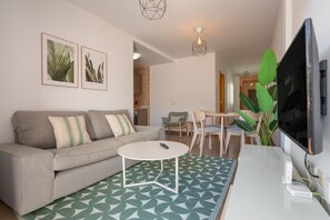 Una sala de estar moderna con un sofá, una mesa de centro, un televisor e impresiones botánicas enmarcadas en la pared.