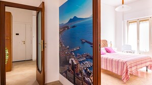 Une chambre à coucher avec un lit, une table de chevet, une lampe et une vue sur le paysage urbain de la côte, visible à travers une grande fenêtre.