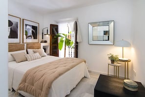 Een slaapkamer met een bed, nachtkastjes, een spiegel en kunstwerken in lijsten aan de muur.