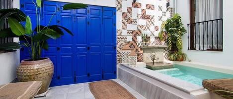 Un área de piscina con una puerta azul, un muro con azulejos y una pequeña fuente.