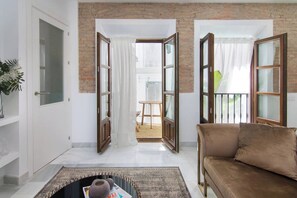 A living room with a brown sofa, a coffee table with a magazine, and a view of a balcony with a wooden railing. - Riad Alhambra 1 (granada)
