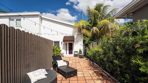 Un patio con dos sillones de mimbre, piso de baldosas y valla de madera.
