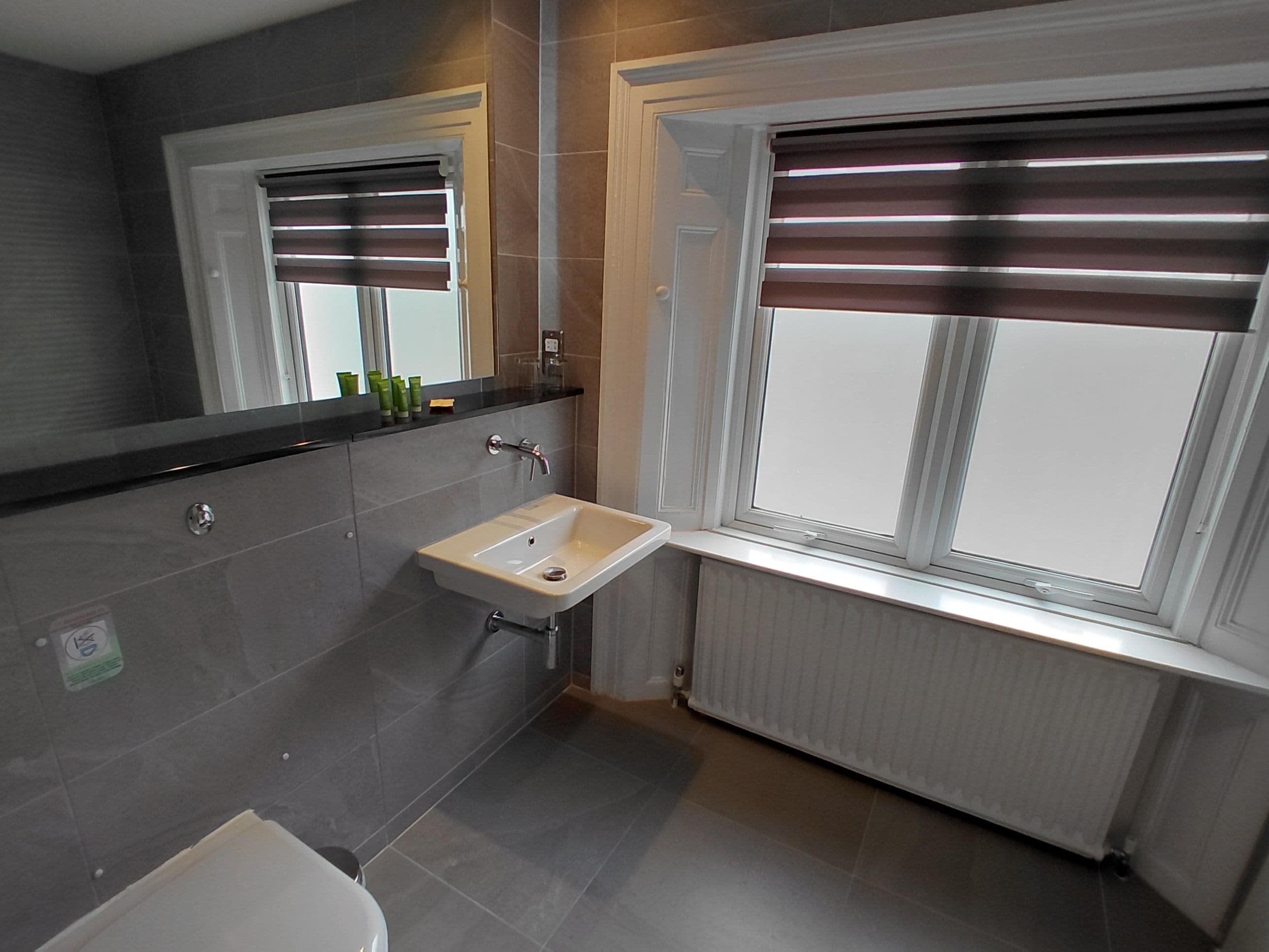 A bathroom with a white sink, a mirror, and a window with blinds.