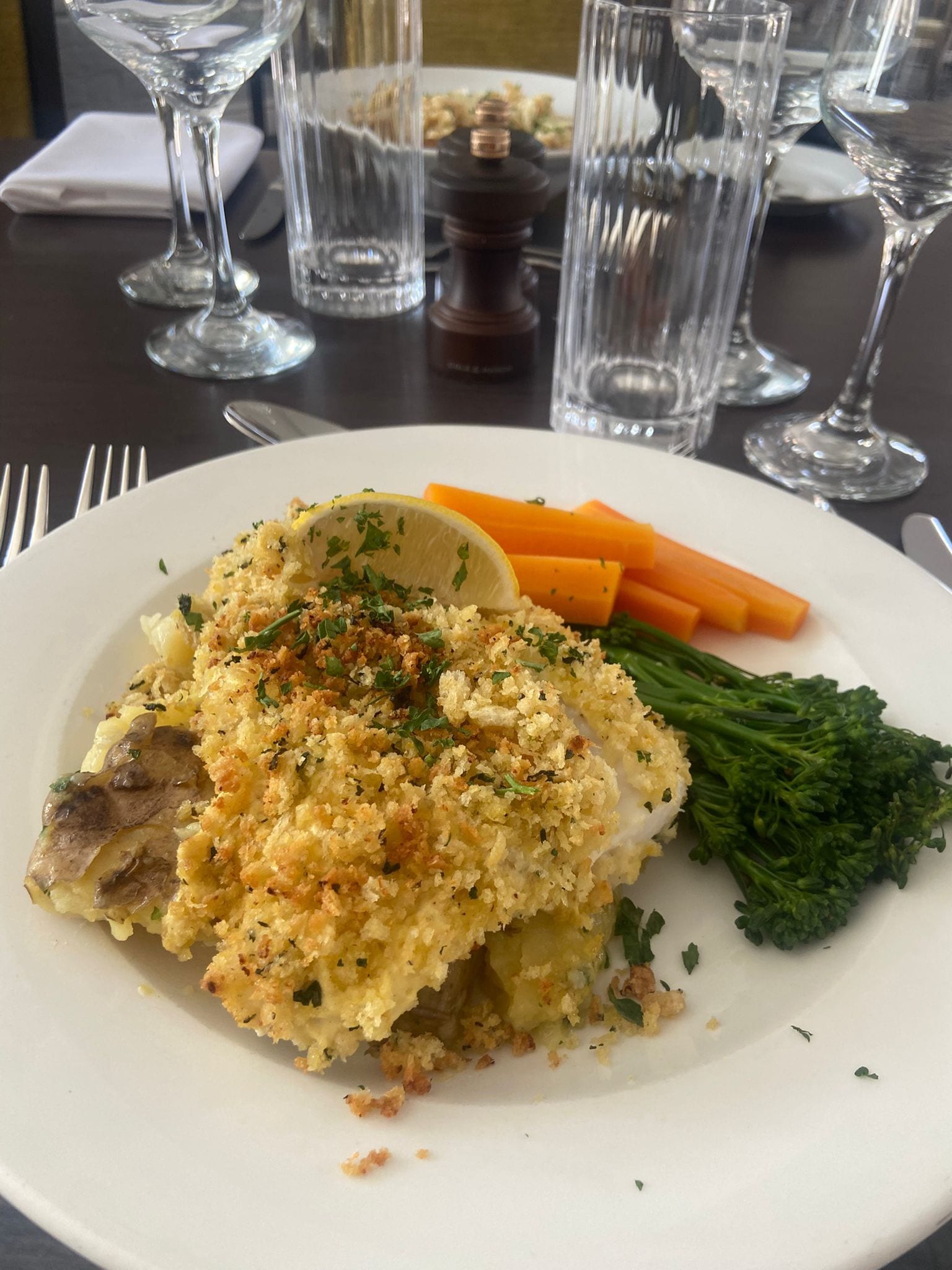 A plate with a breaded chicken breast, lemon wedge, carrots, and broccoli.
