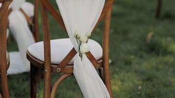 Eine Reihe aus Holzstühlen mit weißem Stoff und floralen Verzierungen, angeordnet auf einer grünen Rasenfläche.
