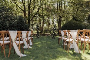 An outdoor seating area with rows of wooden chairs and tables, surrounded by greenery and trees. - Brandon Hall Hotel and Spa (Coventry)