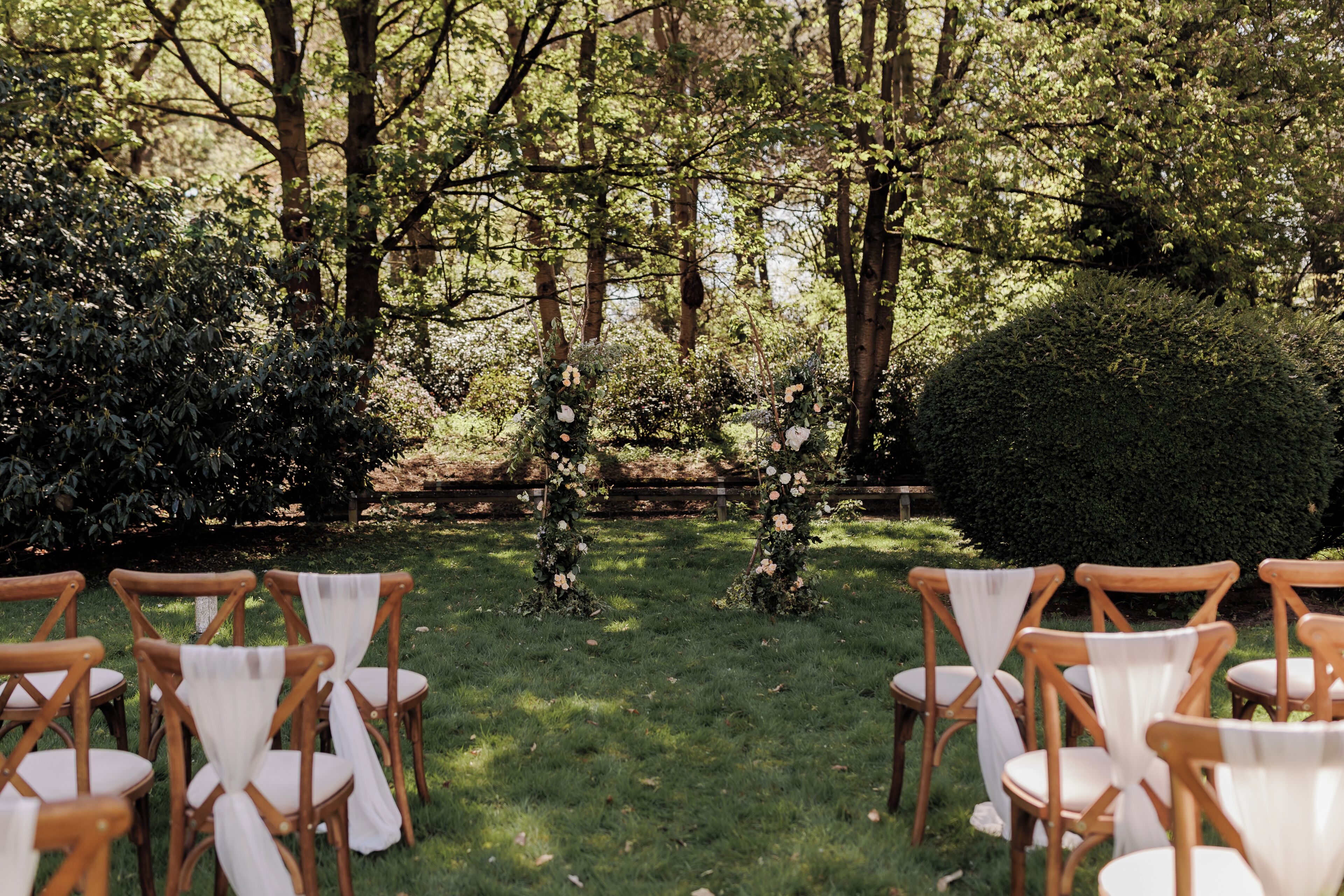 Un espace extérieur aménagé avec des chaises en bois et un sentier bordé de gazon menant à un parterre floral central.