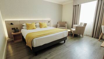 A hotel room with a bed, two chairs, a bedside table, and a large window with curtains.