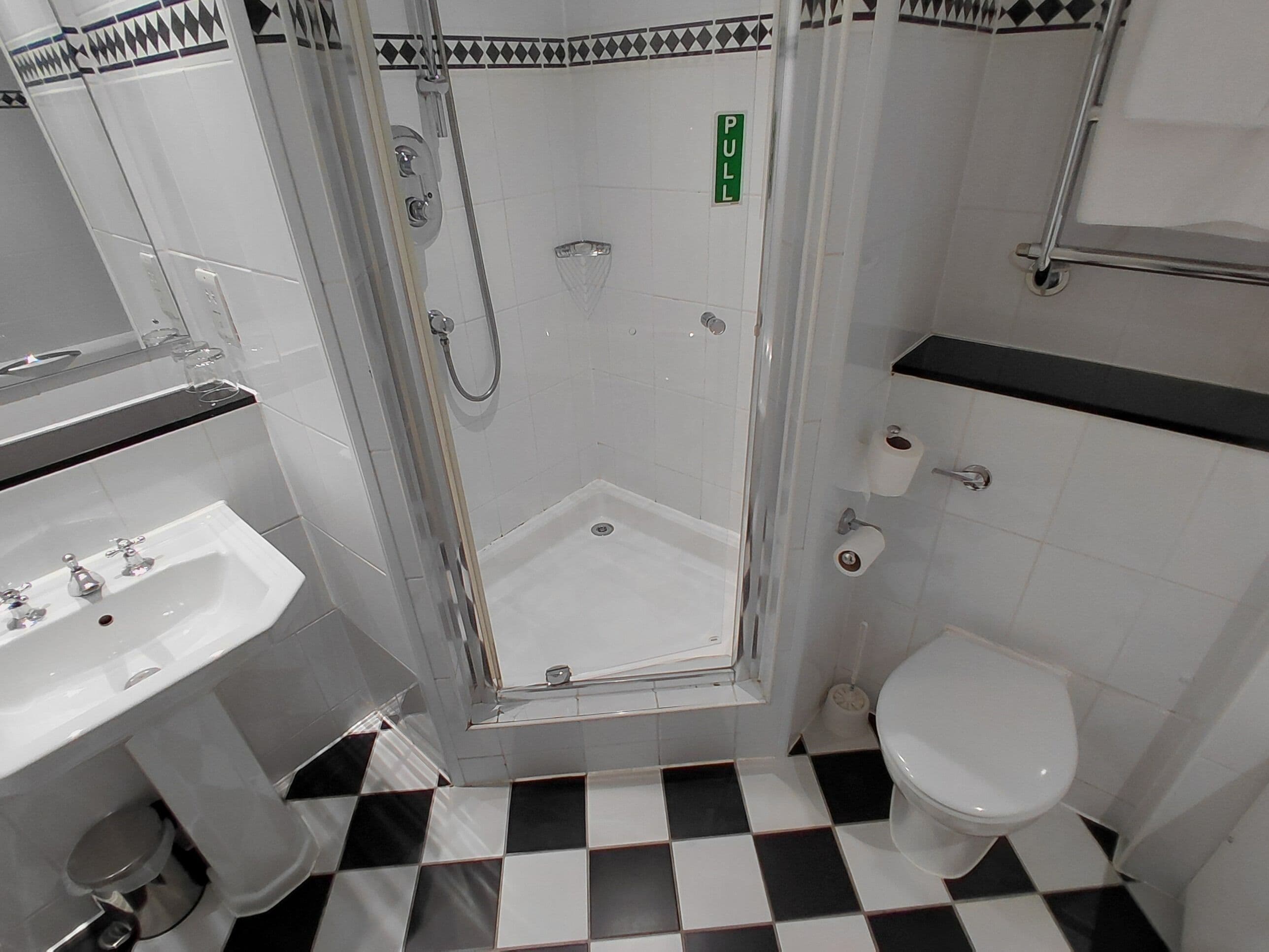 Un baño con ducha, inodoro, lavamanos y suelo con estampado de cuadros.