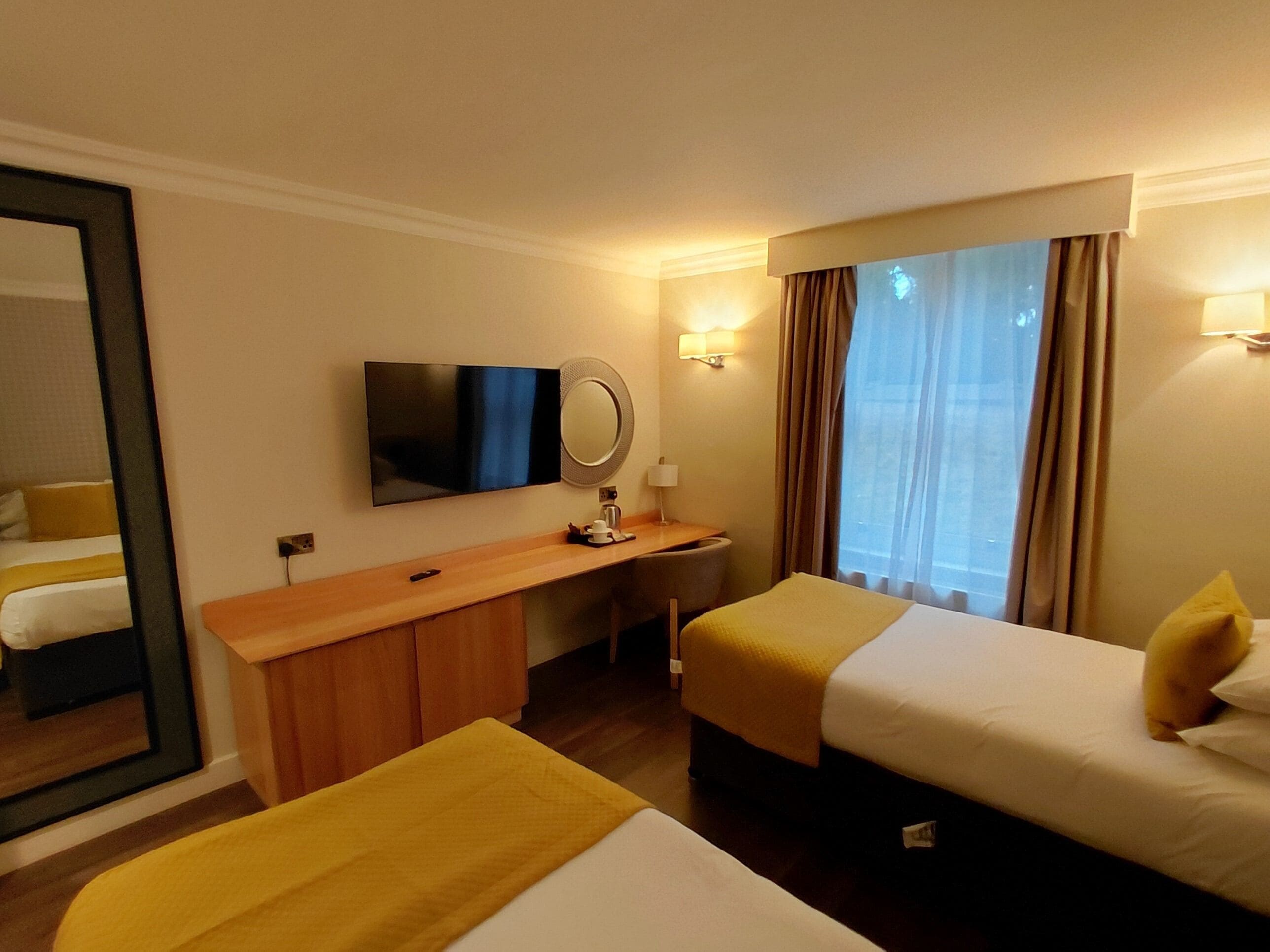 A hotel room with a bed, a desk, a television, a mirror, and a window with curtains.