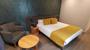 A hotel room with a bed, a chair, a bedside table, and a patterned wall. - Brandon Hall Hotel and Spa (Coventry)