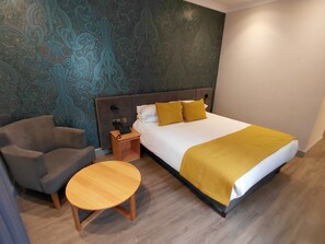 A hotel room with a bed, a chair, a bedside table, and a patterned wall. - Brandon Hall Hotel and Spa (Coventry)