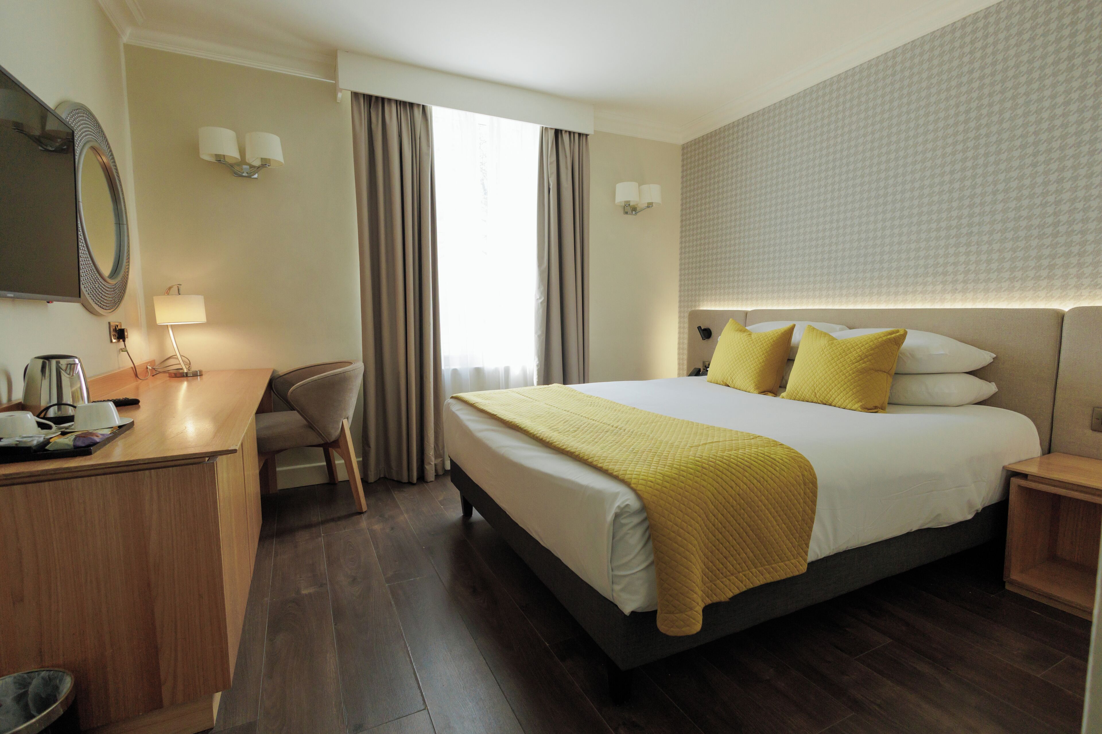 Hotelkamer met een bed, nachtkastjes, een bureau, een stoel, een spiegel en een raam met gordijnen.