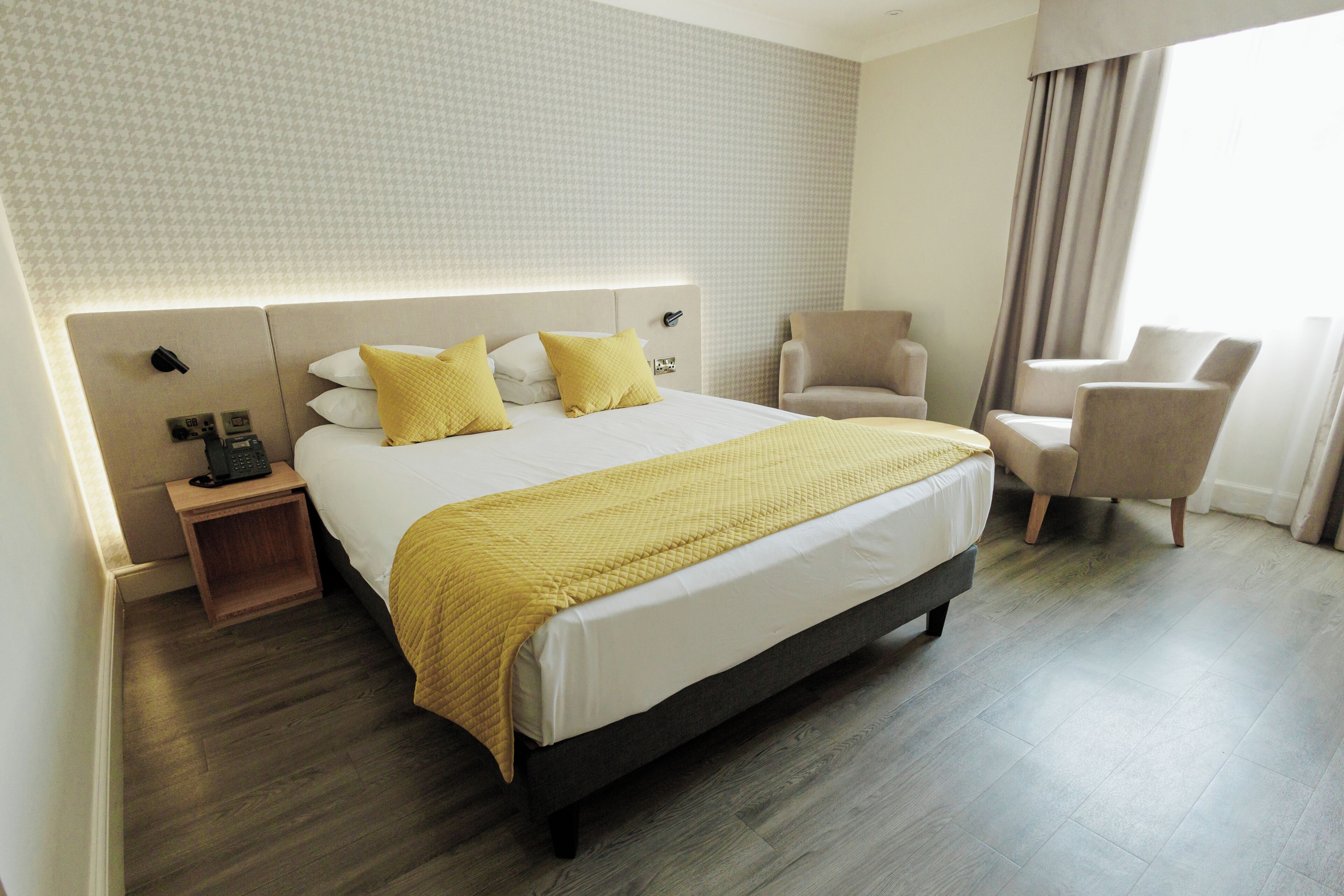 A hotel room with a large bed, bedside tables, a chair, and a window with curtains.