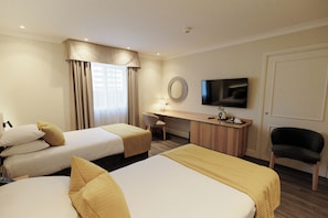 A hotel room with two beds, a desk, a chair, a television, and a window with curtains. - Brandon Hall Hotel and Spa (Coventry)