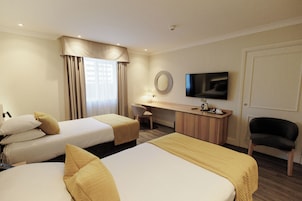 Habitación de hotel con dos camas, un escritorio, una silla, un televisor y un ventanal con cortinas.