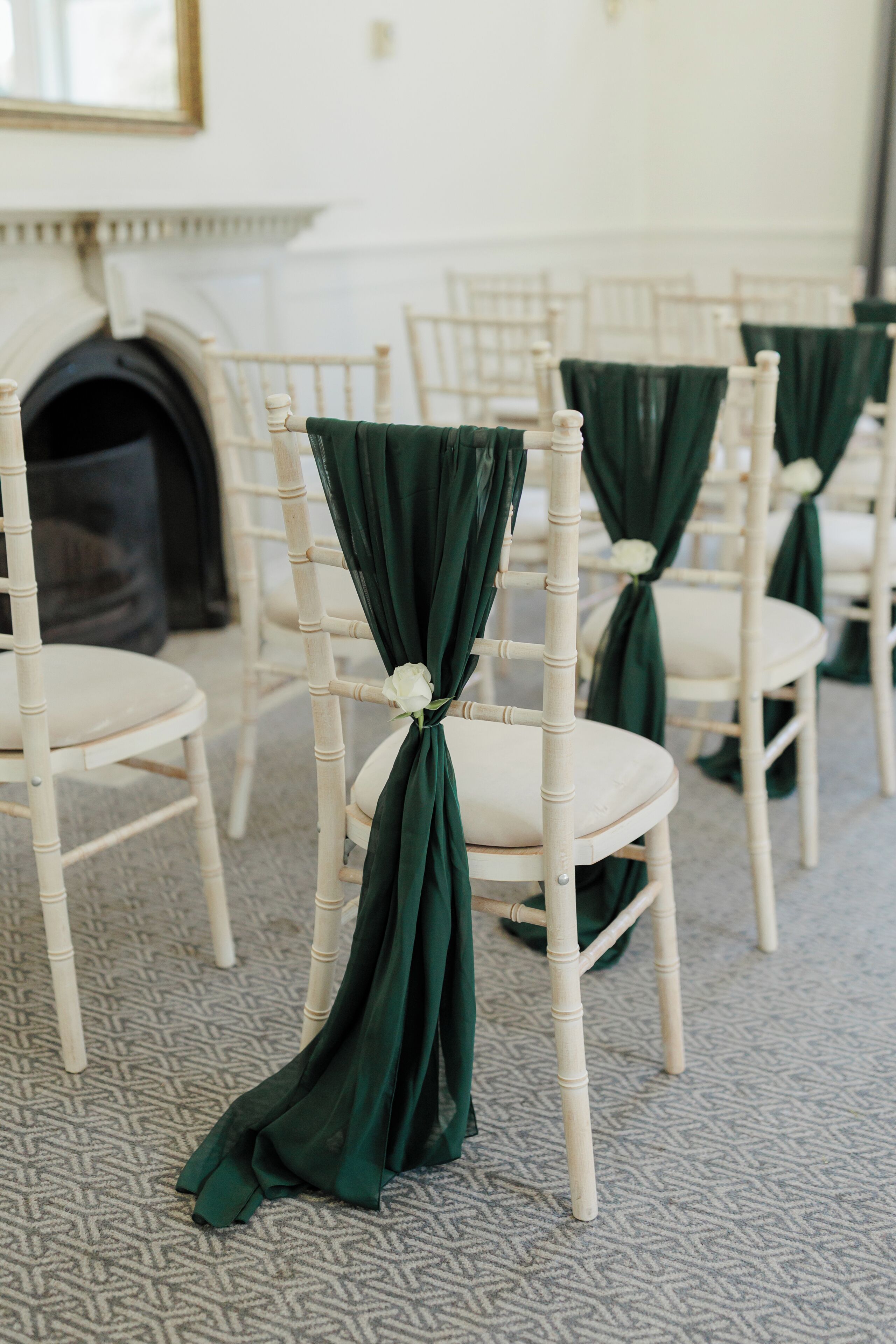 Rows of chairs with green fabric tied at the back, arranged in a room with patterned carpet and a fireplace in the background.
