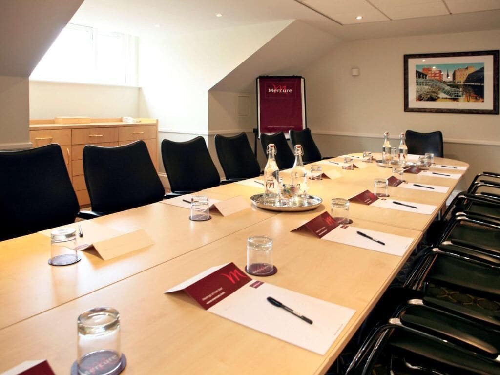 Un salón de conferencias con una larga mesa, sillas, tarjetas de nombre y un banderín.