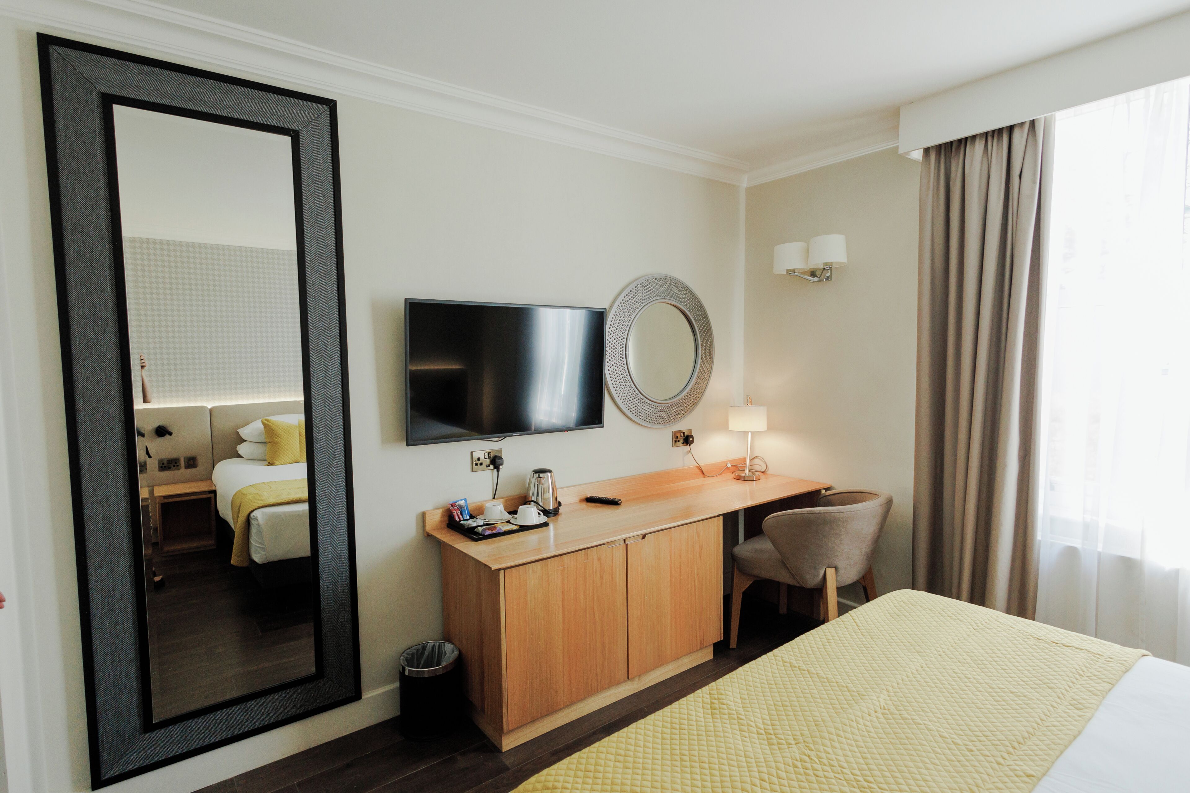 A hotel room with a bed, a desk, a television, a mirror, and a window with curtains.