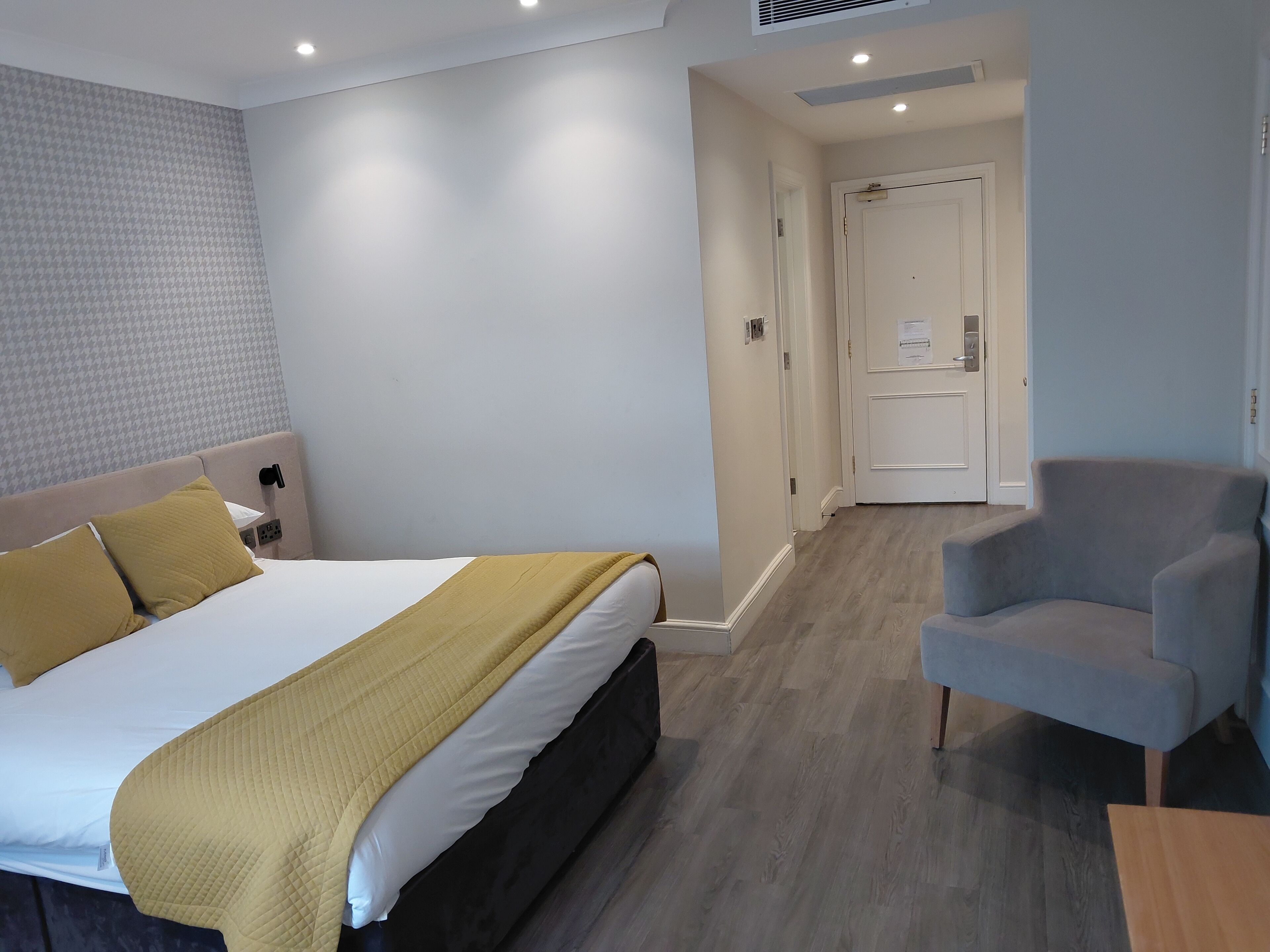Ein Hotelzimmer mit Bett, Nachttisch, Stuhl und einer Tür zu einem anderen Raum.