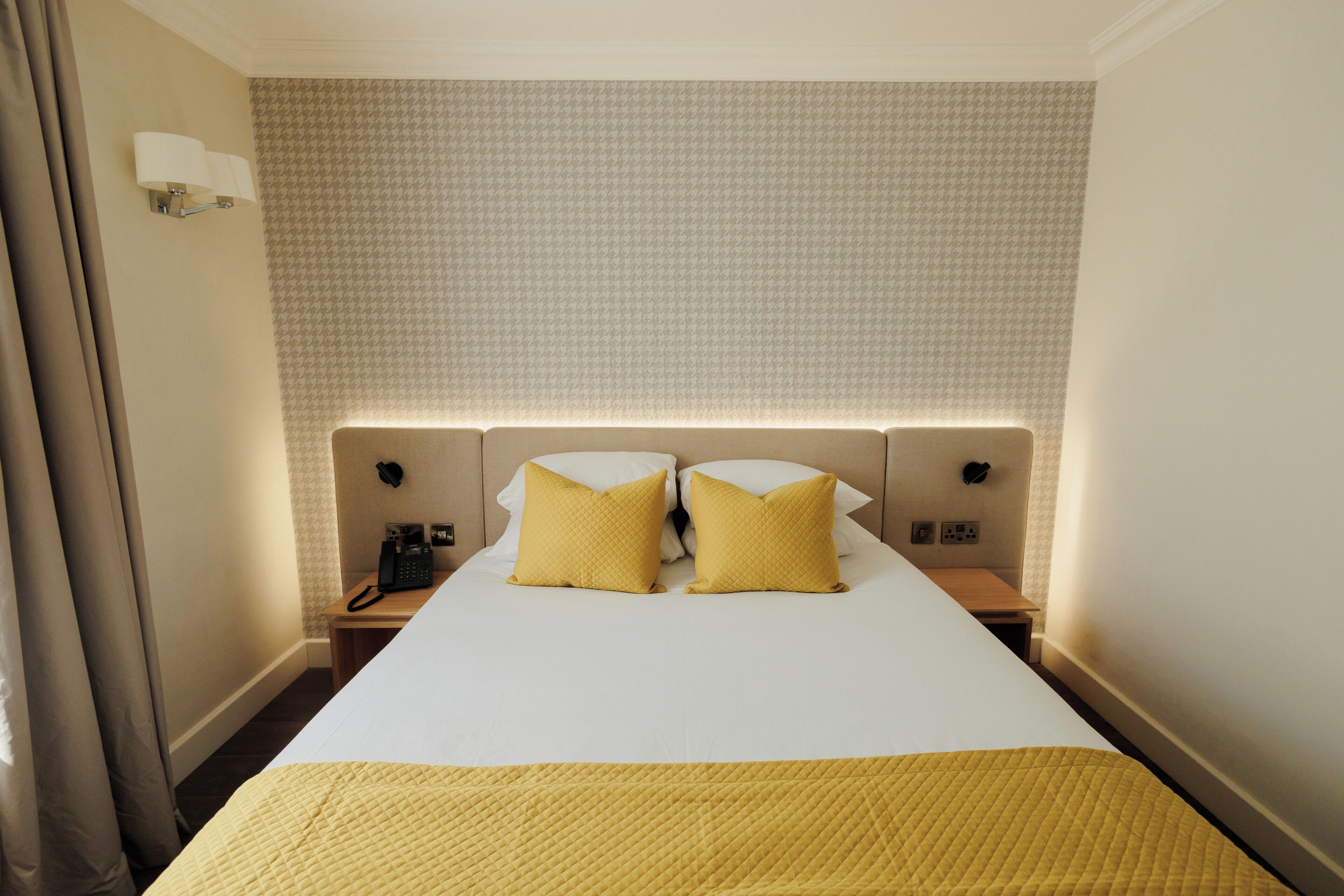 A hotel room with a large bed, two bedside lamps, a telephone, and a wall-mounted light fixture.