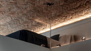 Ein Zimmer mit einem Zargenholzboden-Muster an der Decke, einer Spiegelwand, die ein Bett mit Kissen reflektiert, und einer hängenden Leuchte.