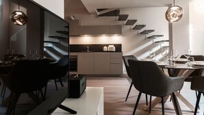 Ein moderner Essbereich mit Fernseher, Esstisch, Stühlen und einer Küche im Hintergrund.