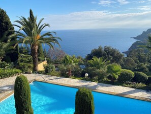 A pool with a view of the sea, surrounded by greenery and a stone pathway. - Villa mit Panorameblick aufs Meer (Théoule-sur-mer)