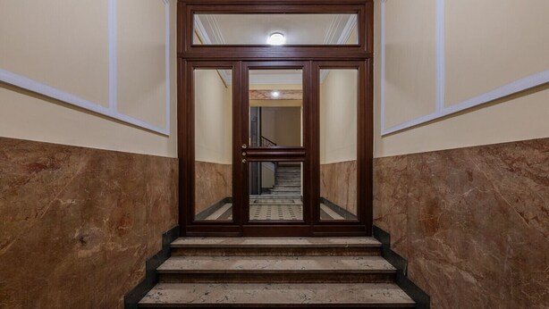 Eine Treppe führt zu einer spiegelnden Tür, am Fuß befindet sich ein roter Teppich.