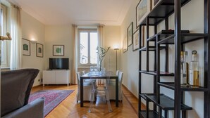 Ein modernes Wohnzimmer mit Essbereich, Holzboden, Fernseher und Bücherregal.