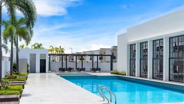 A modern pool area with a clear blue pool, surrounded by white walls and large windows. - Stylish Home via Samborondon - No Pets Allowed (Guayaquil)