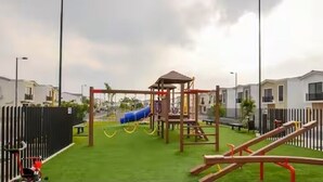 A playground with slides and climbing structures, surrounded by a fence and residential buildings. - Stylish Home via Samborondon - No Pets Allowed (Guayaquil)