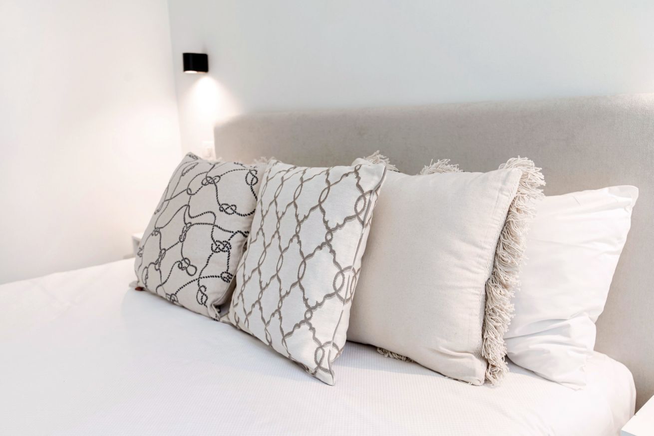 Ein Bett mit zwei Kissen, eines mit Kettenmuster und das andere mit Fransenbesatz.