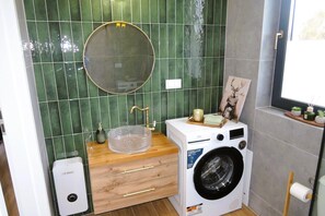 A compact bathroom with a Bosch washing machine, a wooden vanity, a round mirror, and a green tiled wall. - Green Hill Domyslow, 6 persons (Kołczewo)