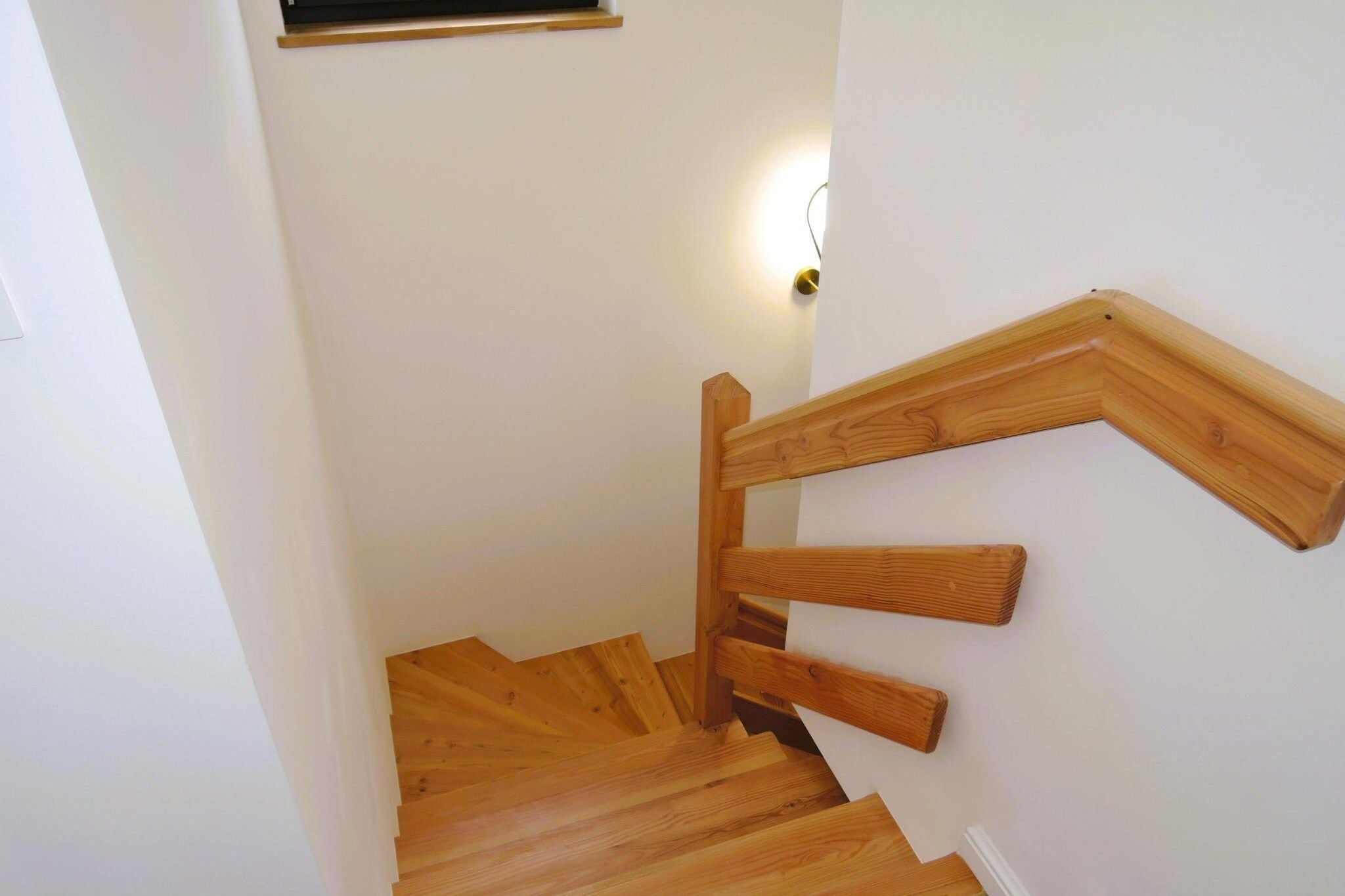 A wooden staircase with a handrail and a light fixture on the wall.