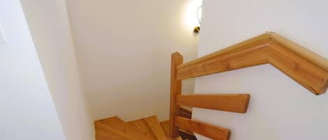 A wooden staircase with a handrail and a light fixture on the wall.