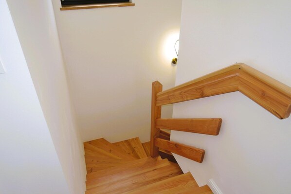 A wooden staircase with a handrail and a light fixture on the wall.