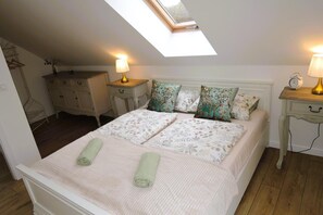 A bedroom with a skylight, a bed with floral bedding, two bedside tables with lamps, and a dresser.