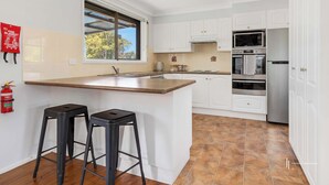 A modern kitchen with white cabinets, a large island with stools, a window with a view, and a fire extinguisher on the wall.