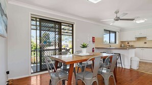 A dining area with a wooden table and grey chairs, a kitchen with white cabinets, and a balcony with a sliding door.