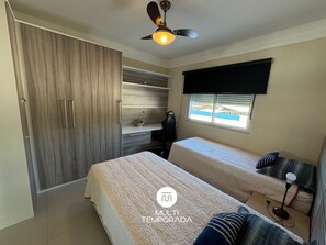 A bedroom with a bed, a desk, a chair, a wardrobe, and a window with blinds. - Dream House Frente Mar - Ponta das Canas (Florianópolis)