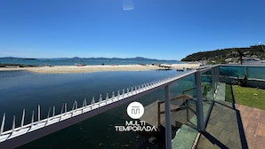Un puente de cristal sobre el agua con vistas claras a una playa y barcos a lo lejos.