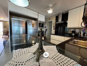 A modern kitchen with stainless steel appliances, a glass-top island, and a decorative Eiffel Tower model. - Dream House Frente Mar - Ponta das Canas (Florianópolis)