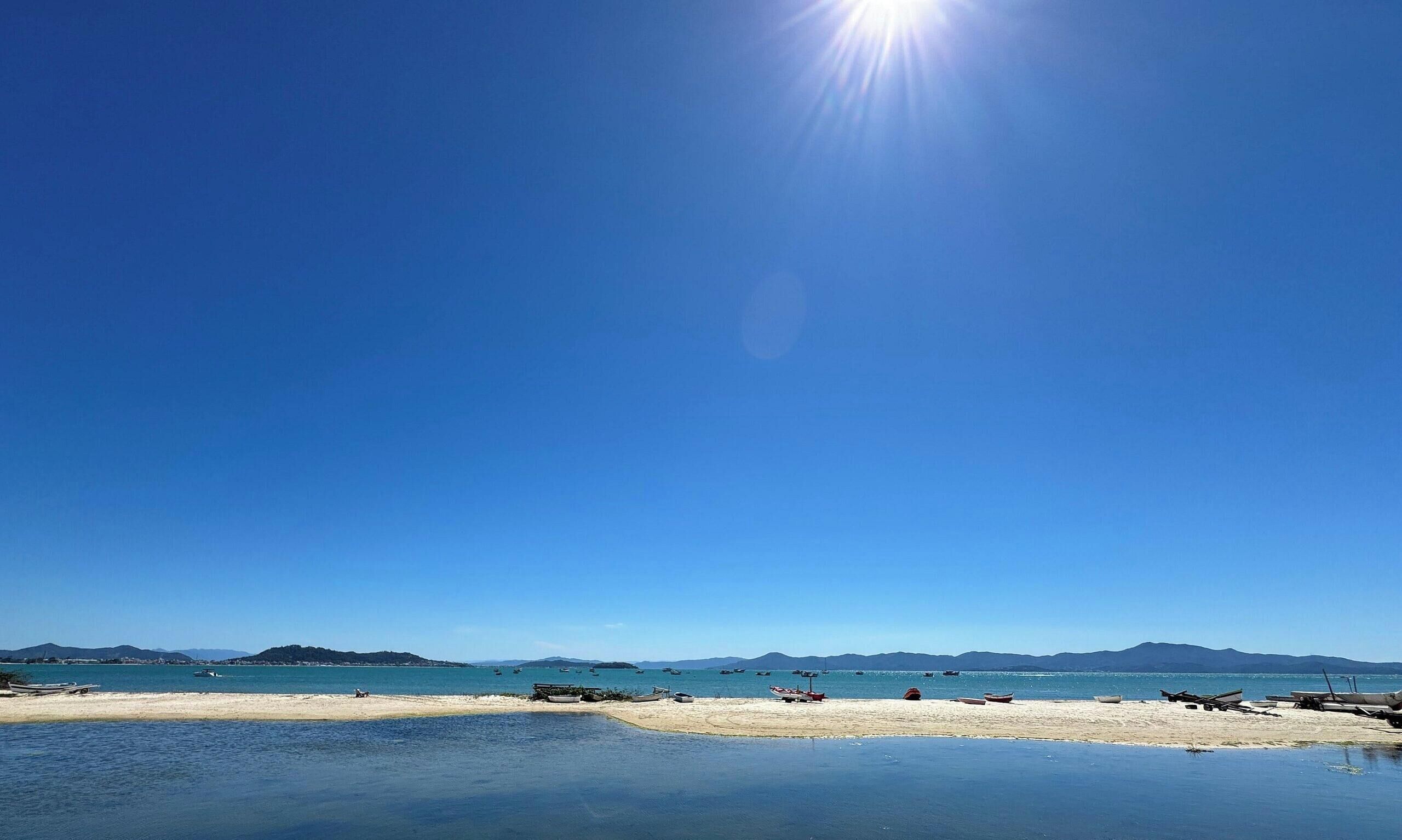 A beach with calm waters, boats, and distant mountains under a clear sky.