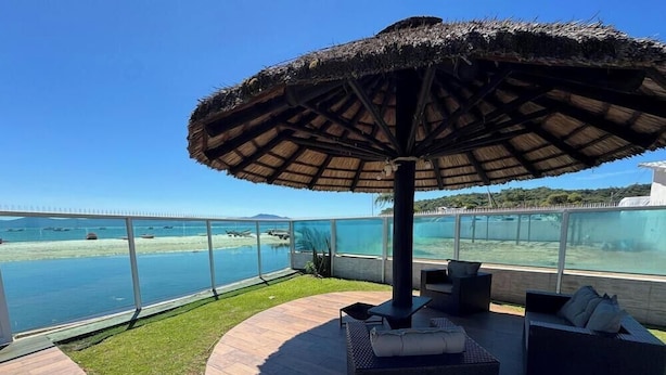 Un espacio de estar al aire libre cubierto, con vista al mar y una isla distante.