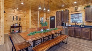 Interno di una baita in legno con un tavolo da pranzo, panche, angolo cottura e una scala.
