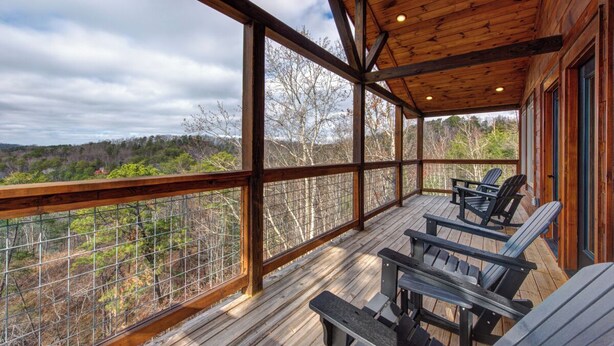 Un terrazza in legno con sedie e tavoli, affacciata su un paesaggio boscoso.